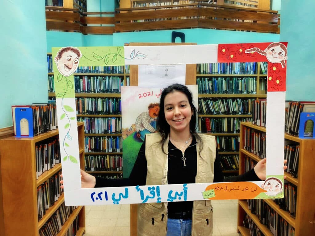 A girl holding a painted frame made of carton.