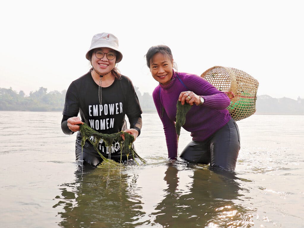 Two women standing in water with a bag on their back.