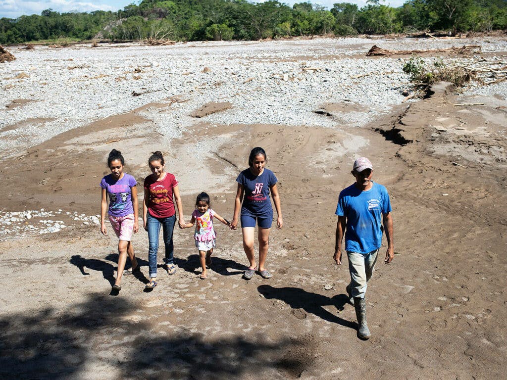 A group of people, adults and children, walking on sandy ground.