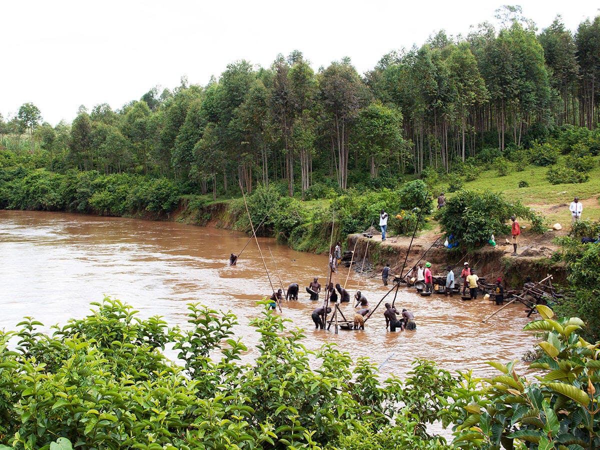 A view over a lake in Kenya and a forest, there are people working by the water.