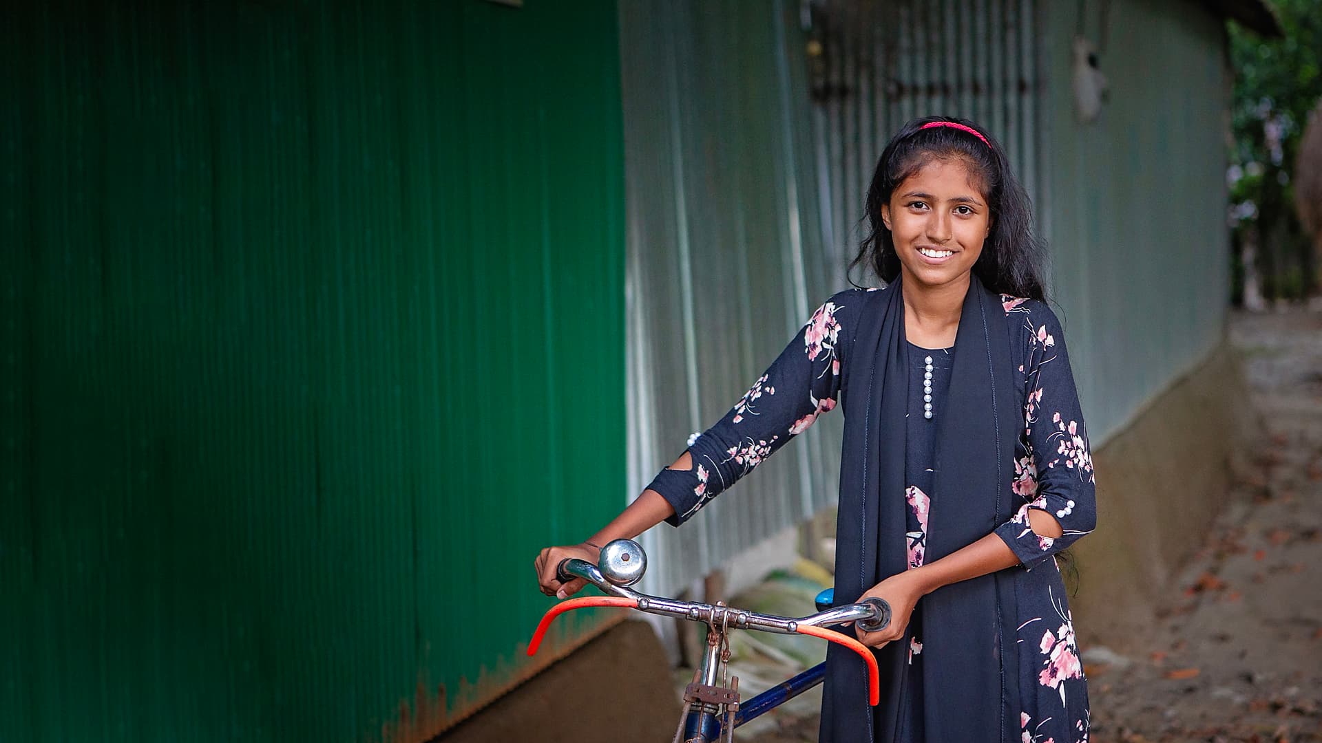 A girl with long dark hair and a dark dress with a bicycle.