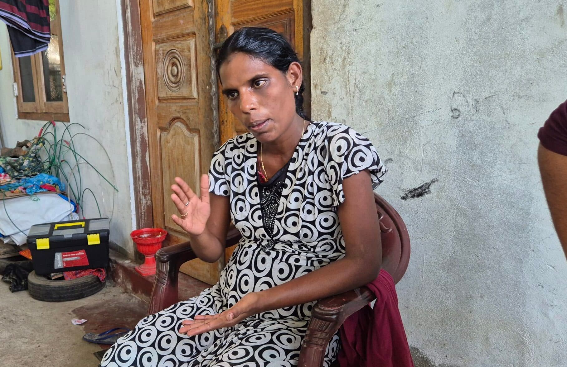 A woman seated indoors, speaking and gesturing with her hand during a conversation.