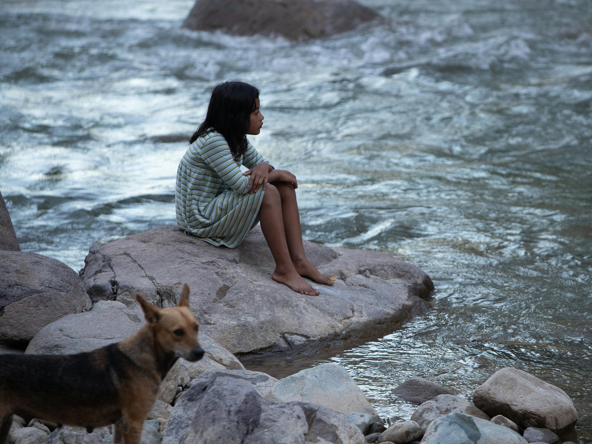 Flicka sitter vid förorenad flod