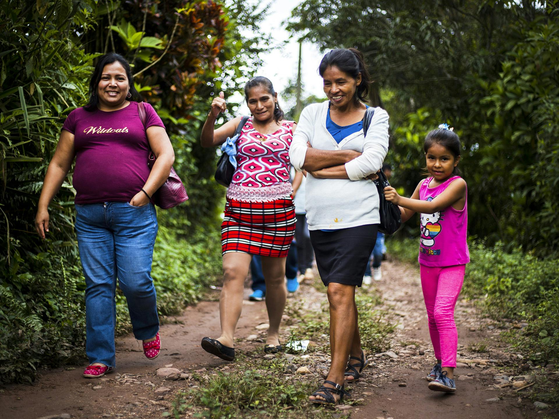 Tre kvinnor och ett barn vandrar på en bred stig i ett skogsområde. De ser glada ut.
