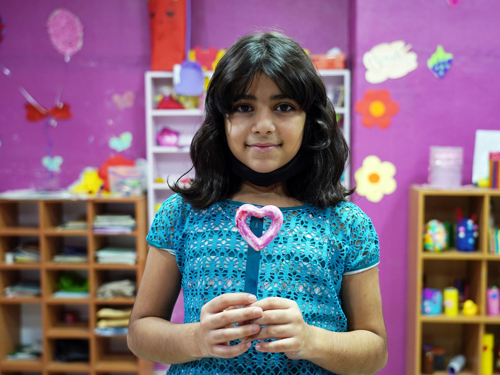 En flicka står i ett rum med färgglada bilder och håller ett pysselhjärta