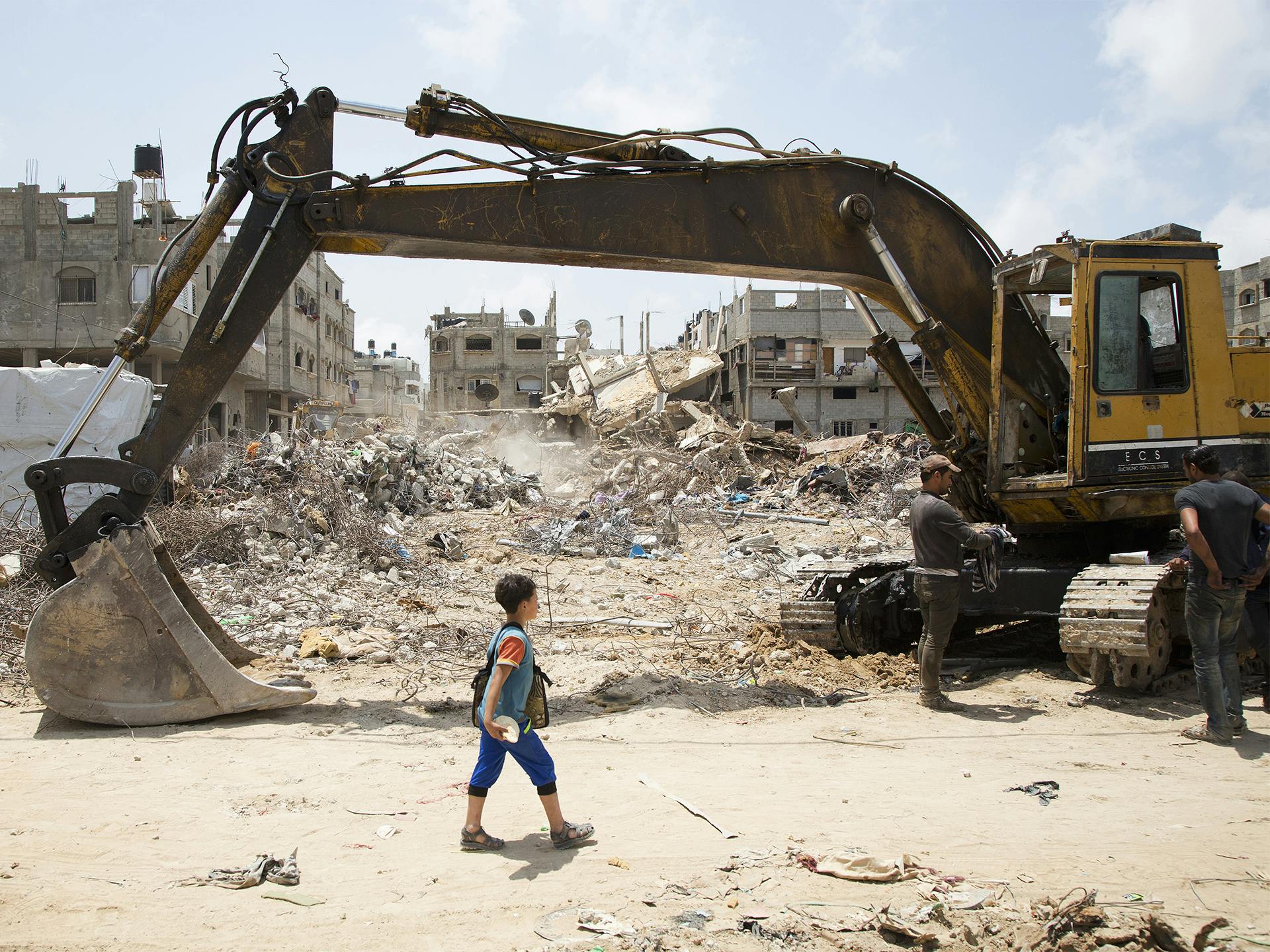 Pojke framför ruiner och grävskopa i Gaza