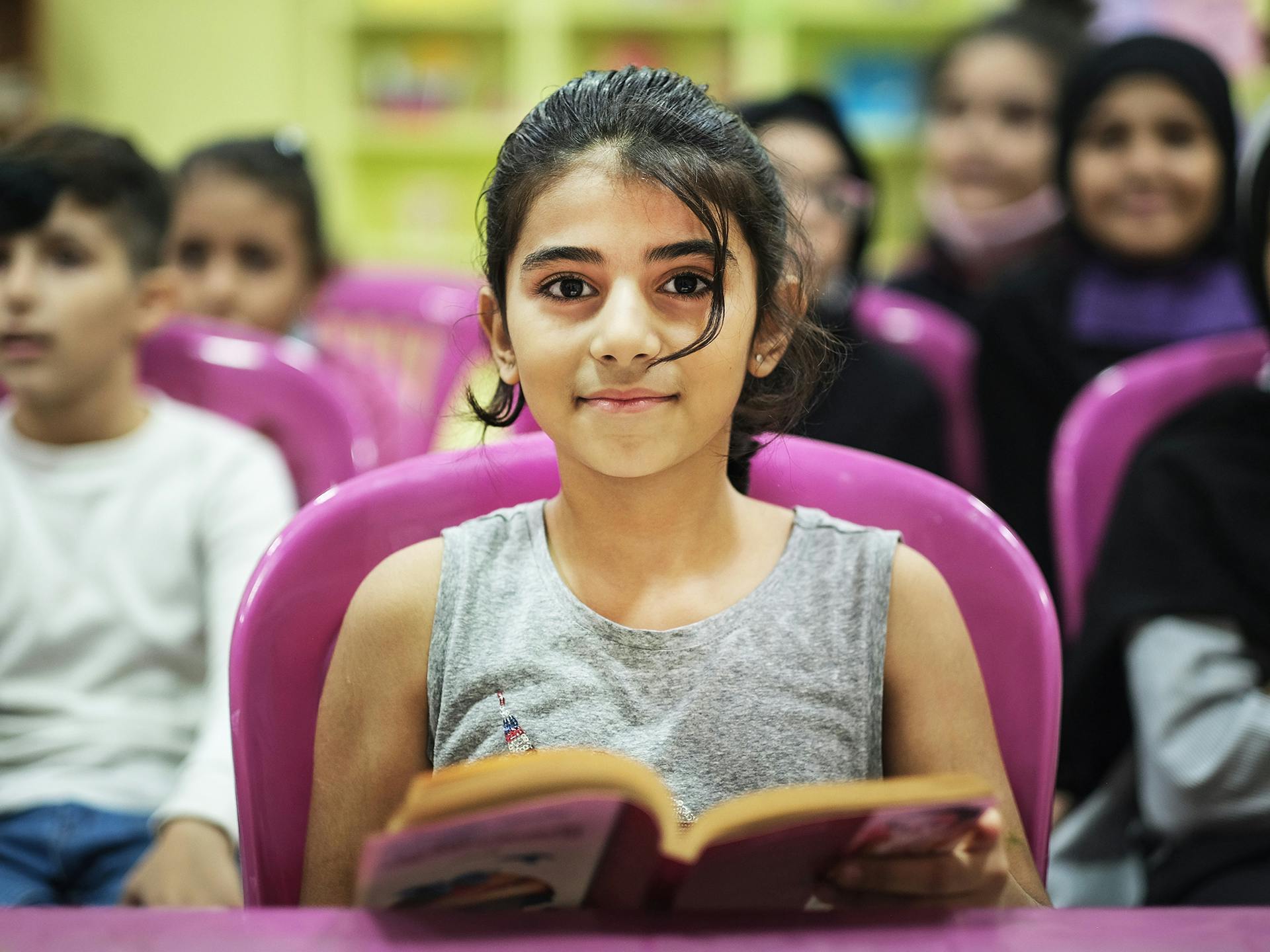 En flicka i ett klassrum med en bok i händerna.