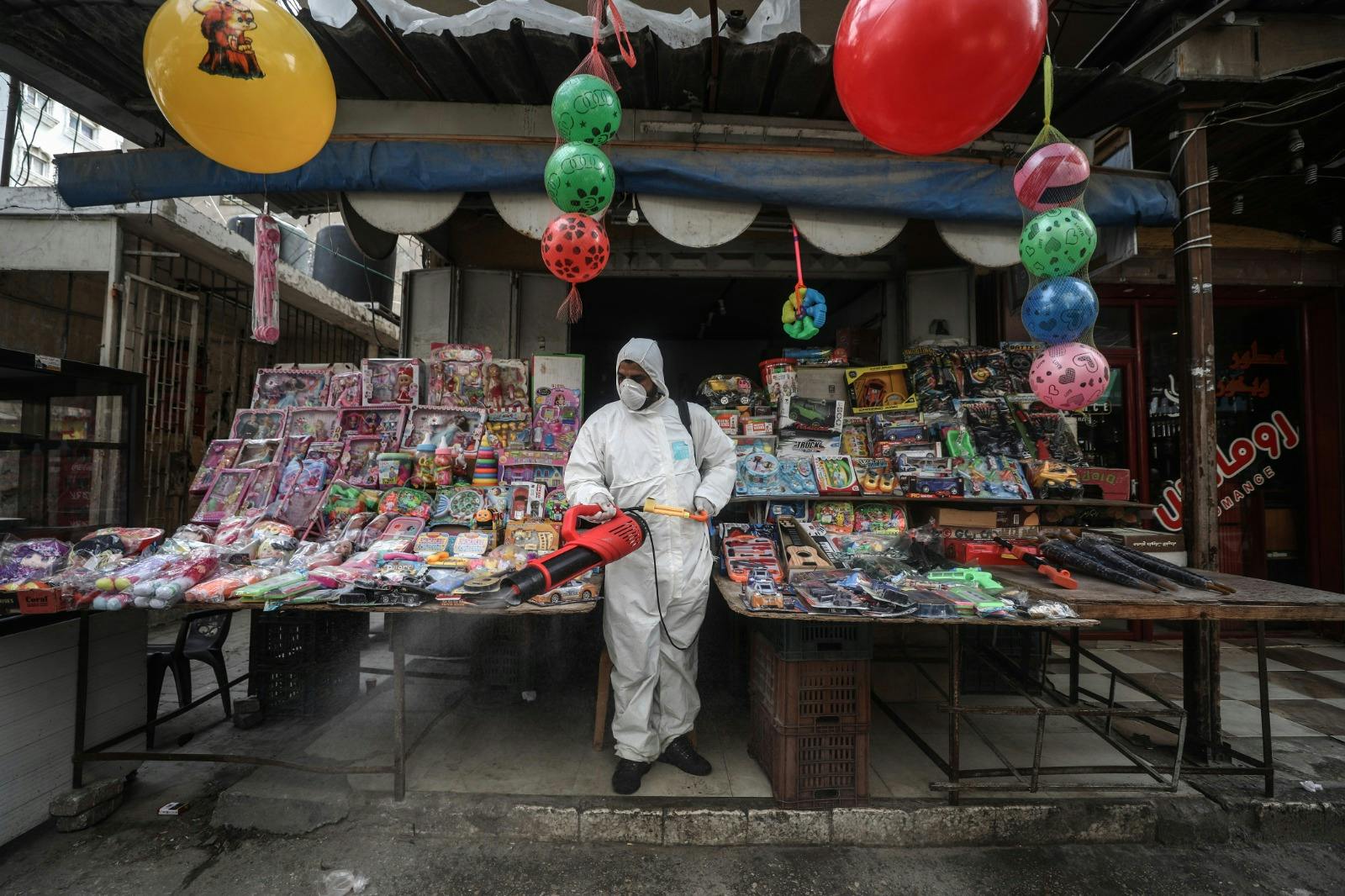 A health worker in protective suit sanitising a market stall.