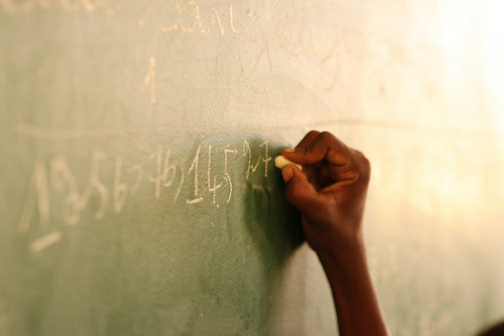 A hand writing with chalk on a blackboard.