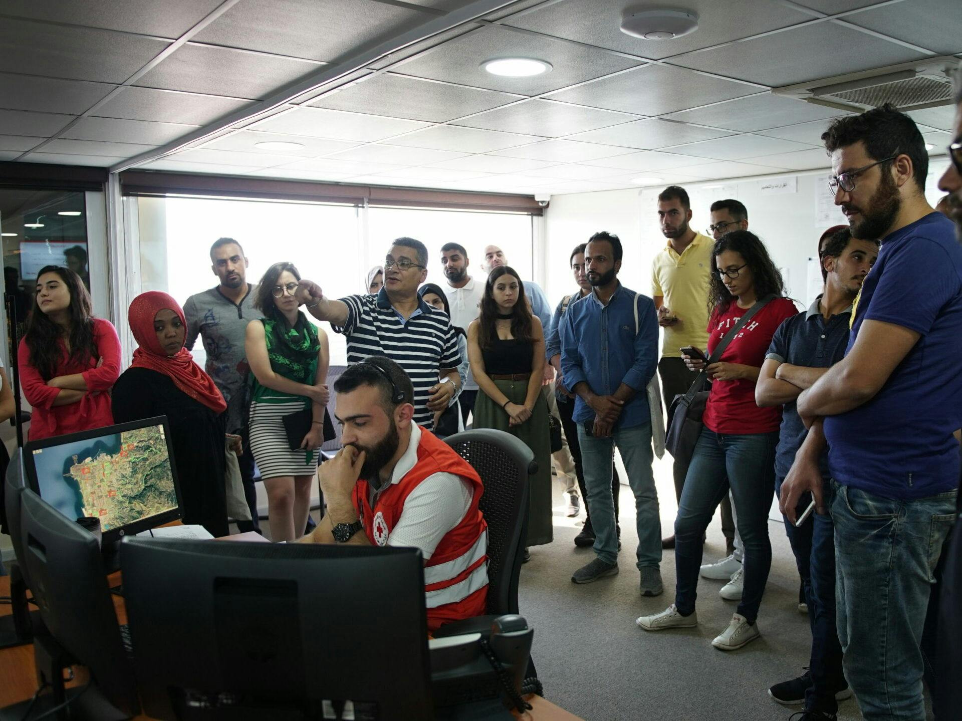 A group of people observing the work of an emergency coordinator in front of many computer screens.