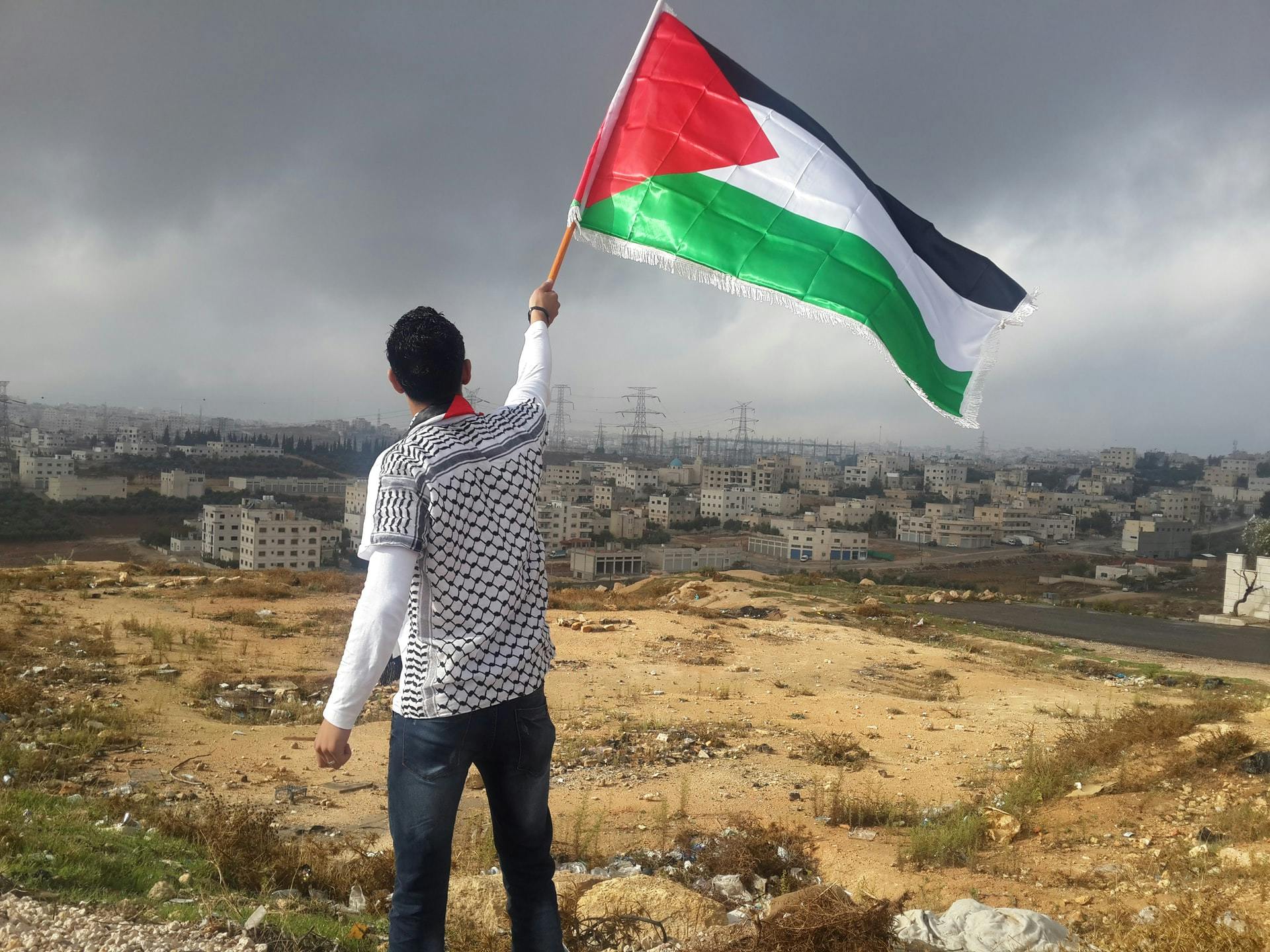 A young man waving a Palestinian flag. In the background Palestinian houses.