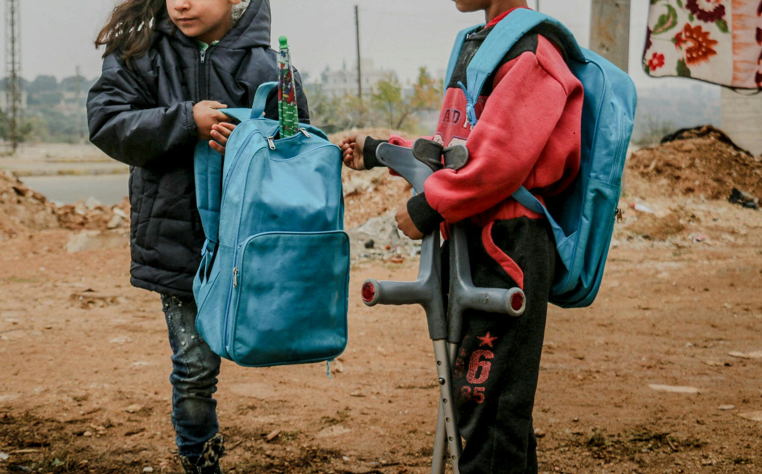 A boy helping a girl on crutches carrying her school bag in Idlib, Syria.