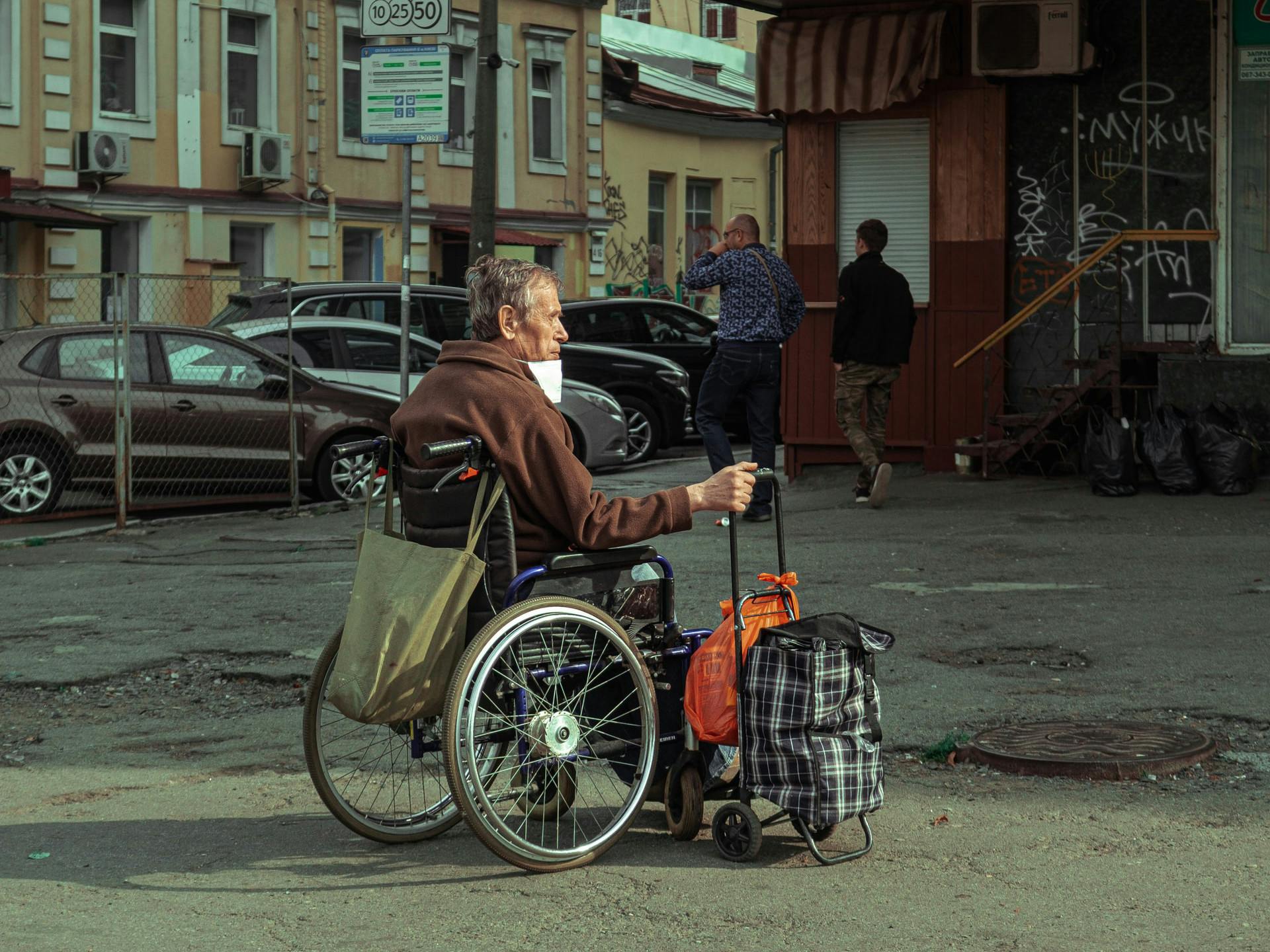 A man in a wheelchair with a suitcase on a square in Kiev.