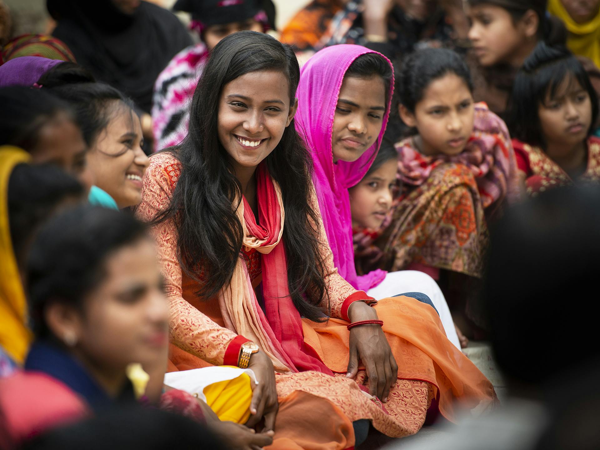 A woman sitting in a crowded group of people, smiling.