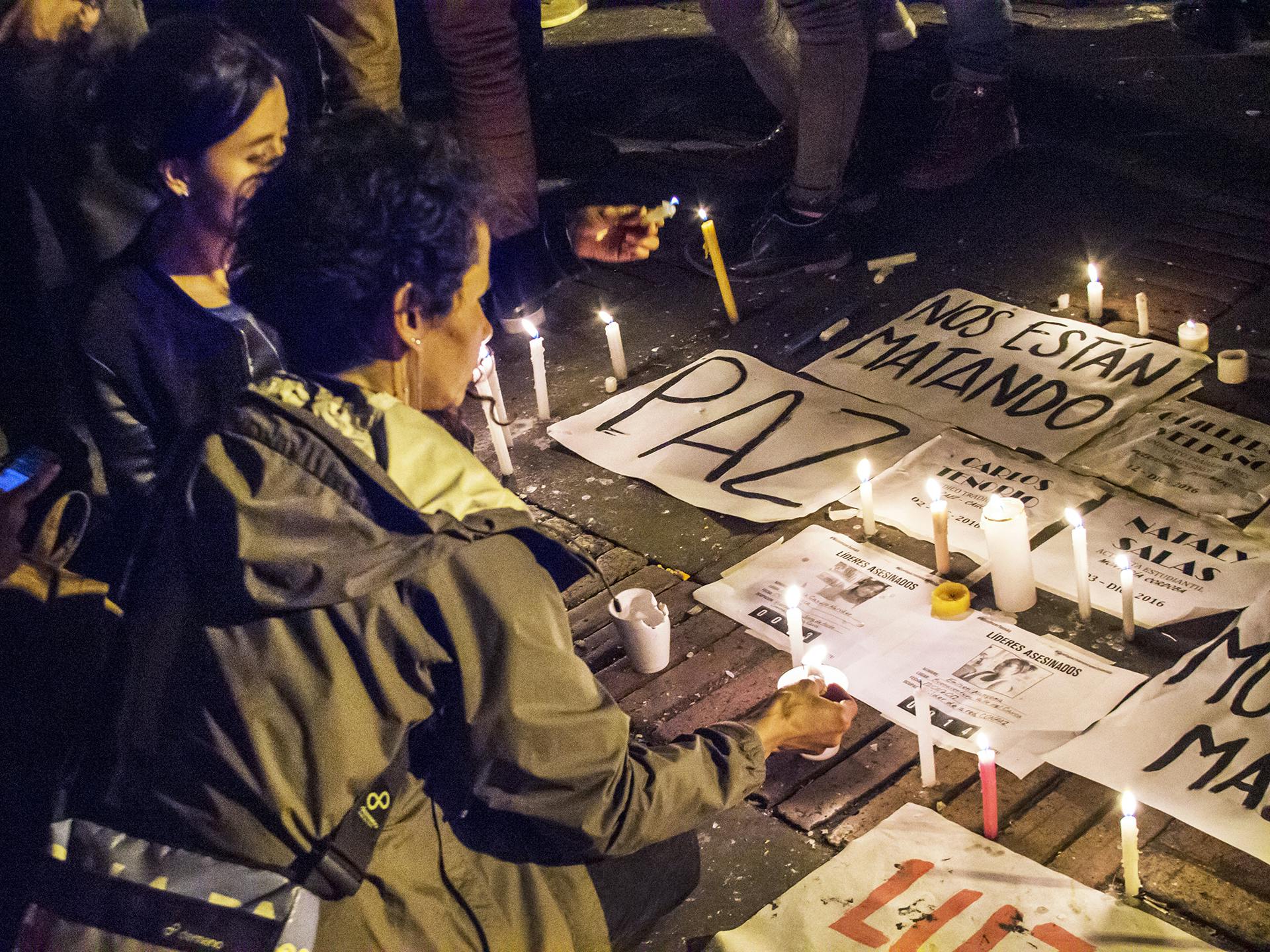 Two women lighting candles next to signs promoting peace.