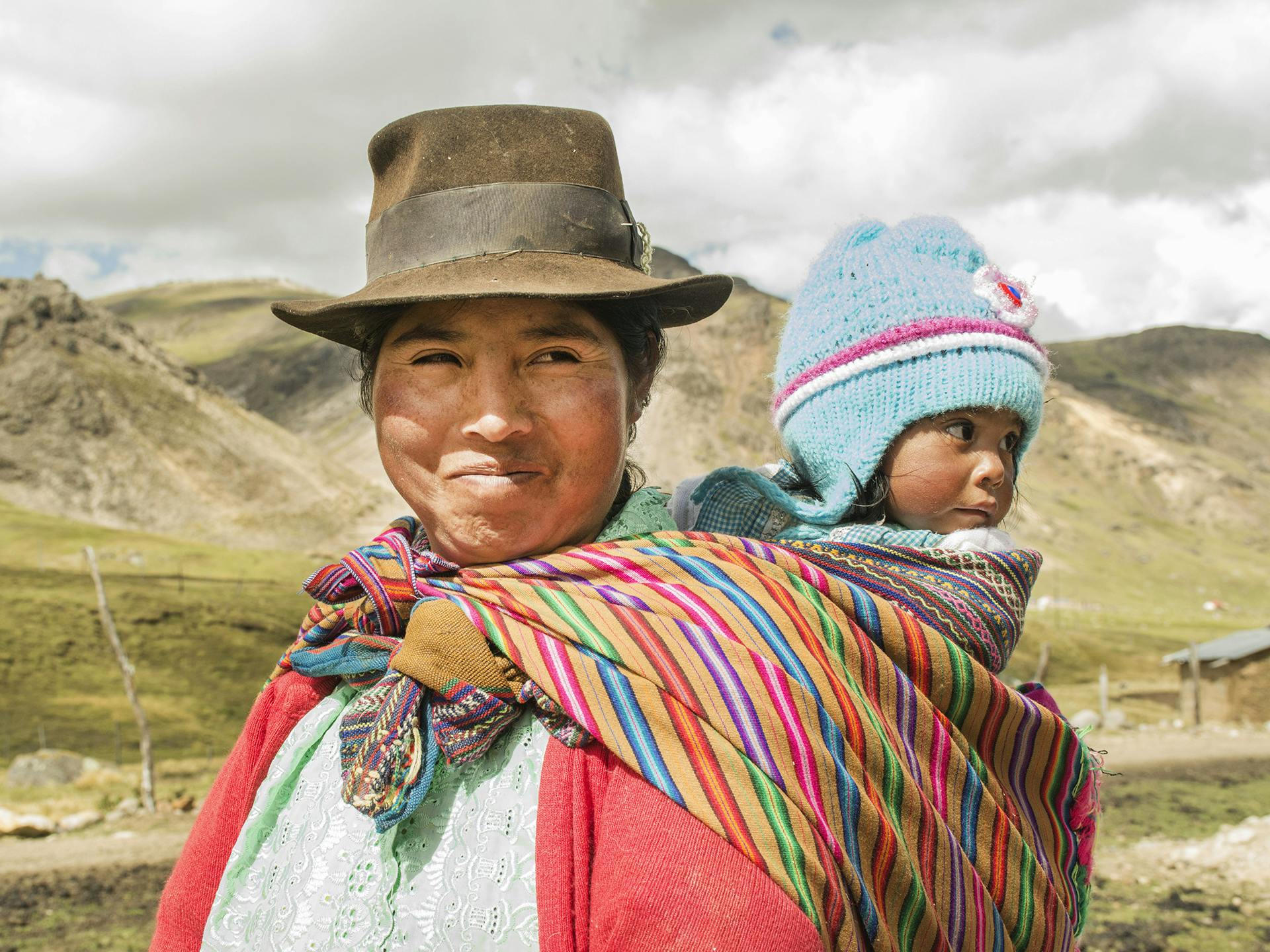 A Peruvian woman in a hat wearing a baby on her back.