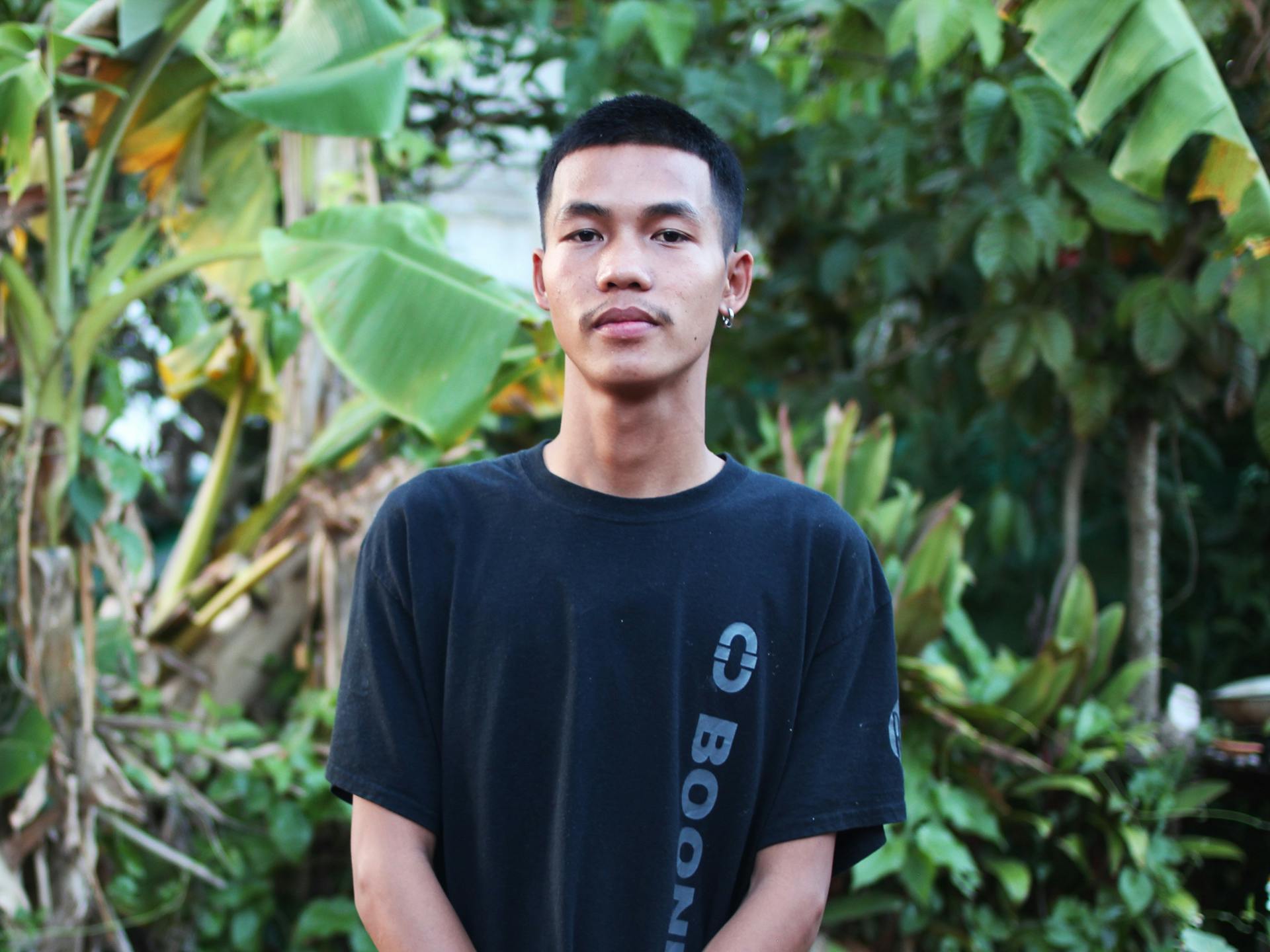 A young Thai man standing with trees behind him.