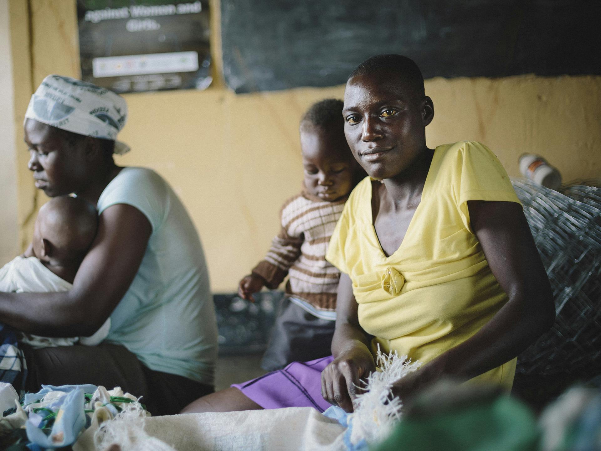 A Zimbabwean woman sitting on a floor sewing with her baby next to her.