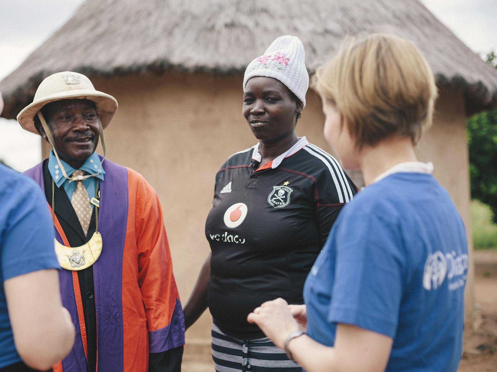 A person wearing a Diakonia t-shirt talking to a Zimbabwean couple.