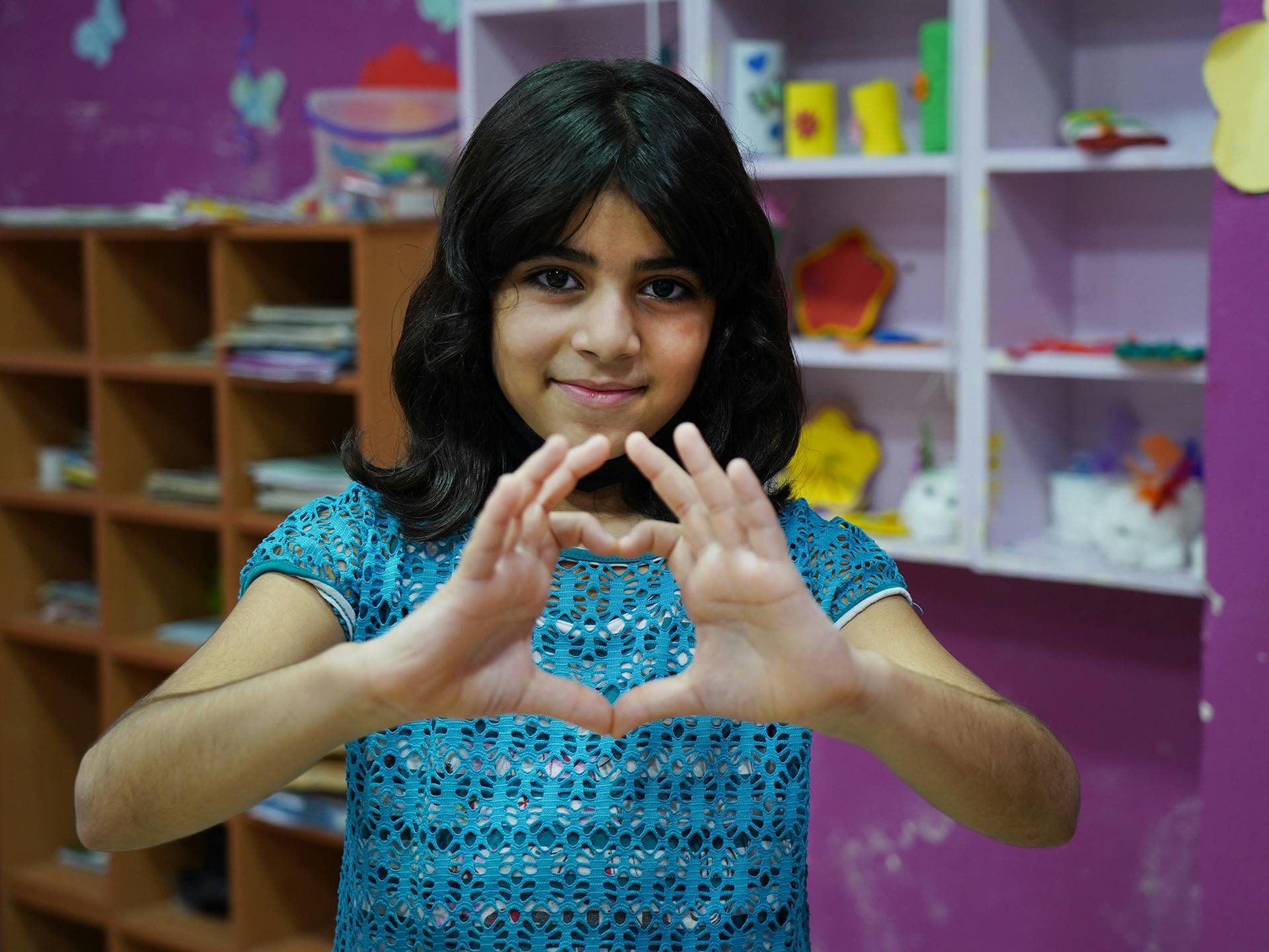 A young girl is holding up her hands to the shape of a heart.
