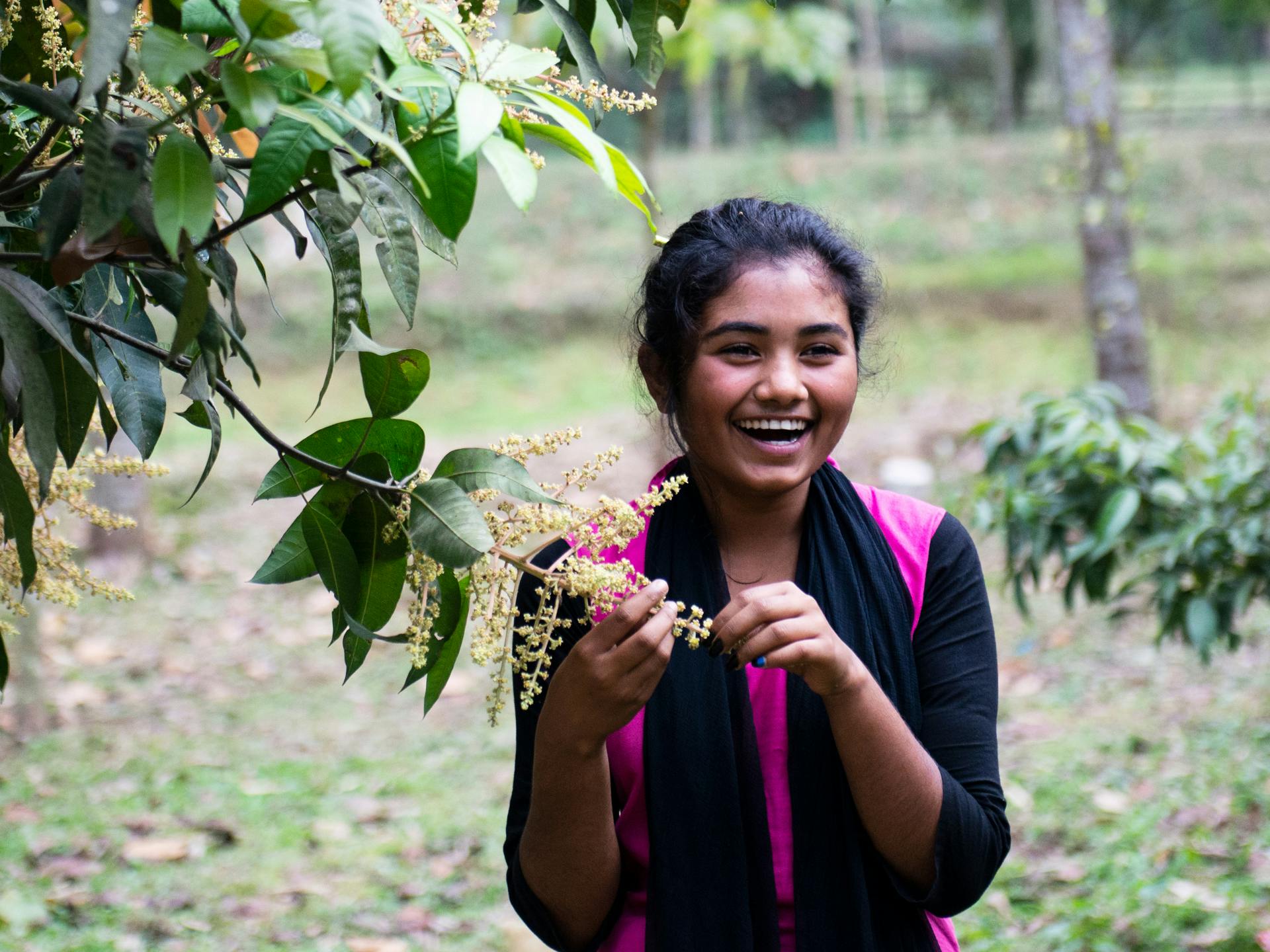 A young woman standing next to a tree, laughing.